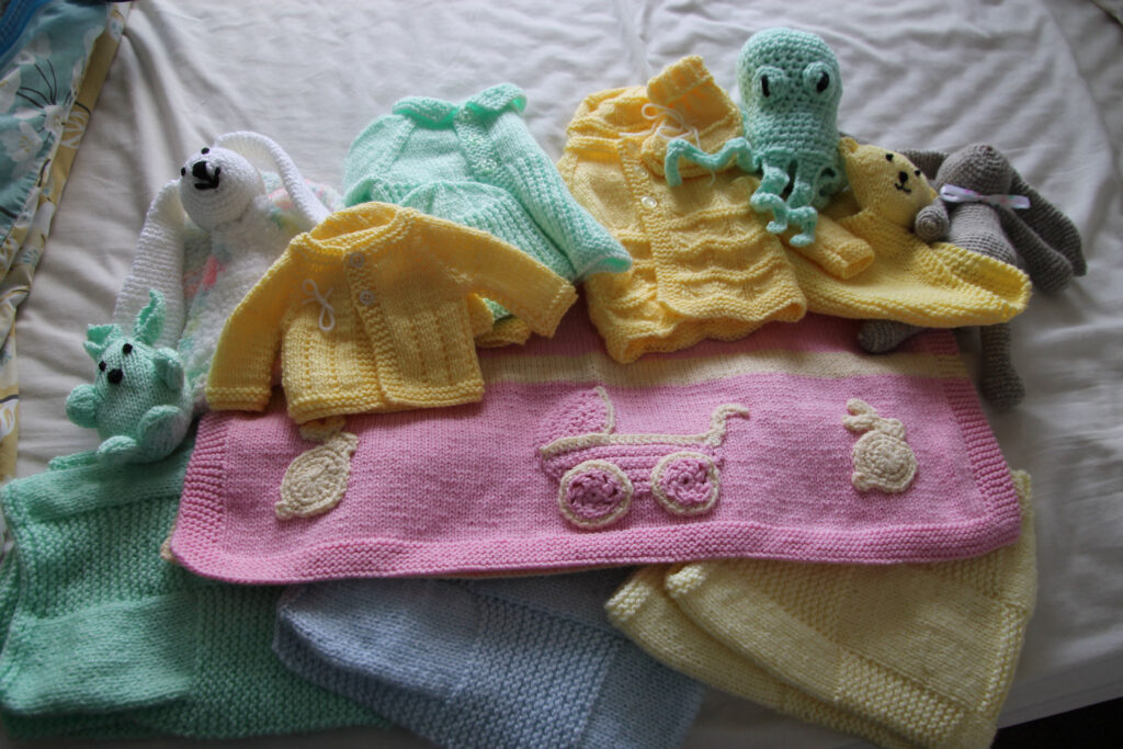 Layette for a baby including blankets, cardigans and soft toys.